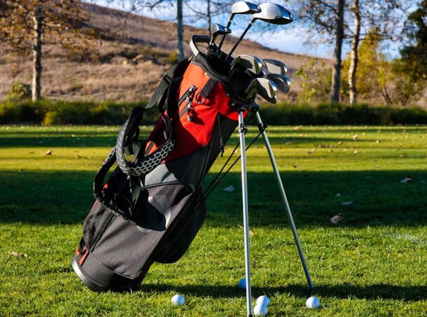 A golf bag with clubs rests on a lush green field under clear blue skies.