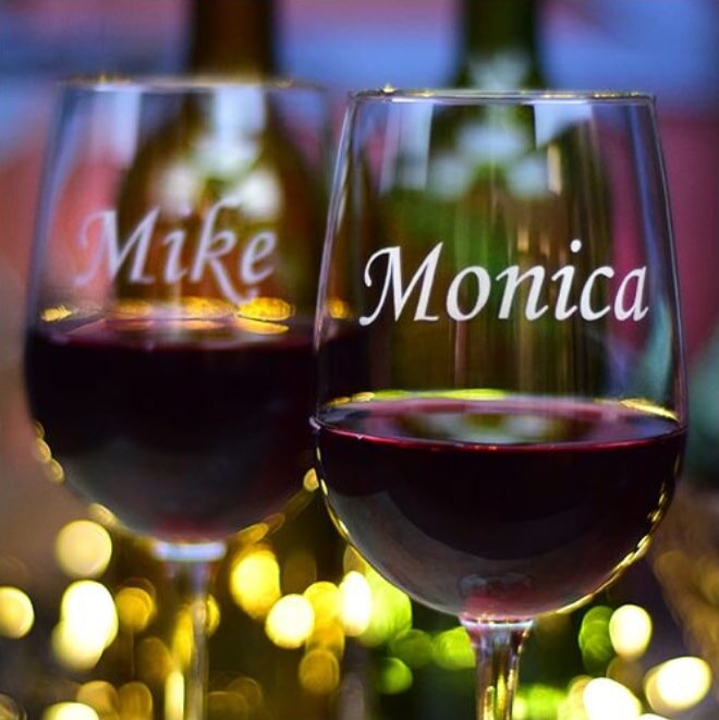 Two wine glasses labeled with the names "Mike" and "Monica" sit elegantly on a table.