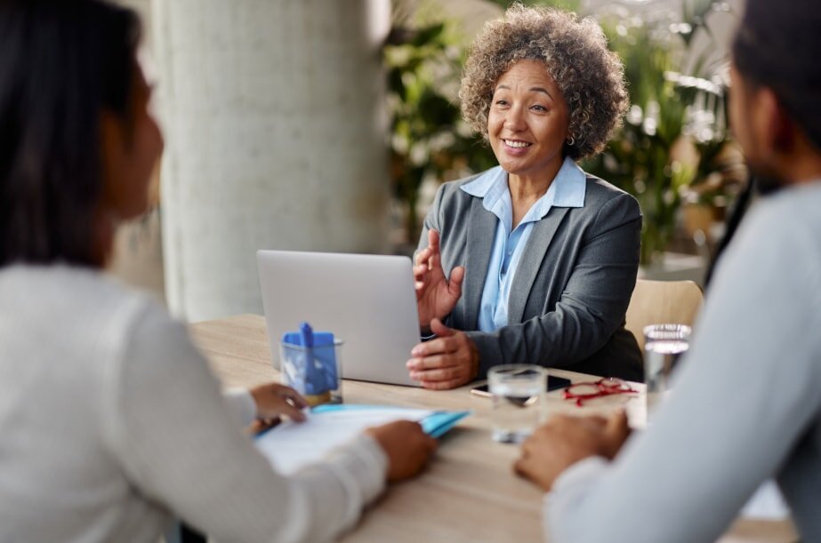 A woman engages in conversation with two people seated at a table.