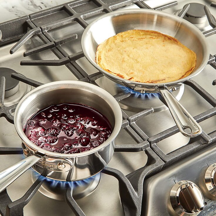 Two pans on a stove top, one filled with simmering blueberry sauce, the other empty and ready for use. 