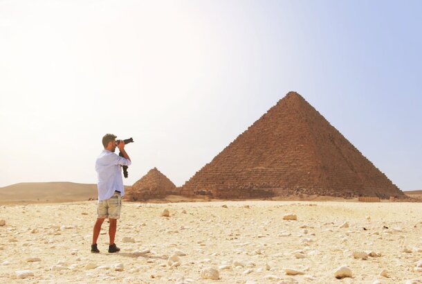 A man photographs the pyramids, capturing their grandeur against a clear blue sky.