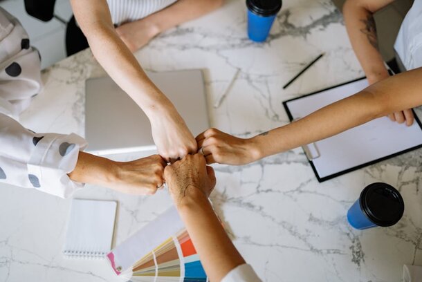 Four people of diverse backgrounds holding hands around a table, symbolizing unity and togetherness.