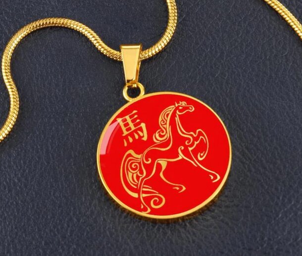 Gold pendant with a red circular design featuring a stylized horse and Chinese character, signifying elegance and cultural symbolism, on a smooth black surface.