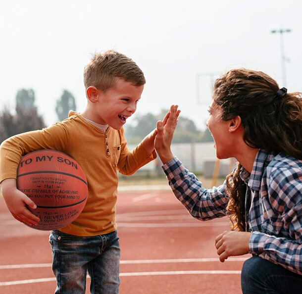 A mother and son joyfully playing basketball outdoors, showcasing their bond and active lifestyle.