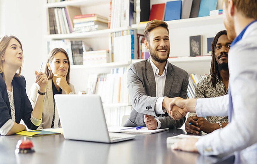 A group of diverse individuals seated at a table, engaging in handshakes to signify agreement or collaboration.