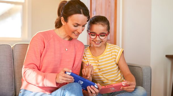 A woman and a girl joyfully playing together with a Nintendo Switch console in a cozy living room setting.