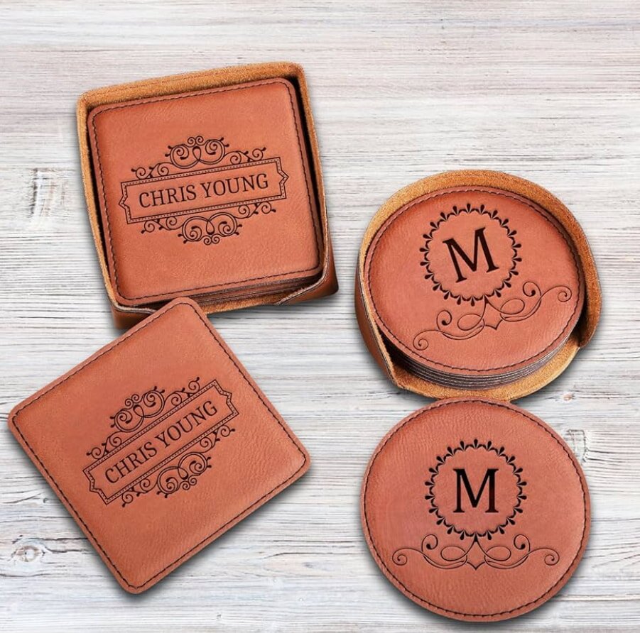 Leather coasters on a wooden table; square ones labeled "Chris Young" and round ones with an "M" monogram, featuring elegant scroll designs.