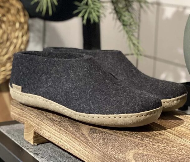 A pair of black felt slippers resting on a wooden shelf, showcasing their soft texture and simple design.