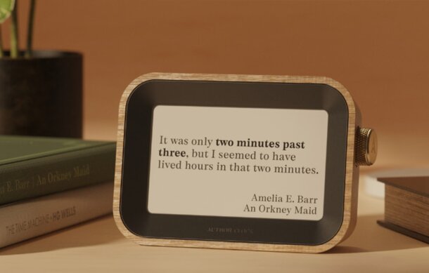 A book resting on a table beside a digital clock displaying the time.