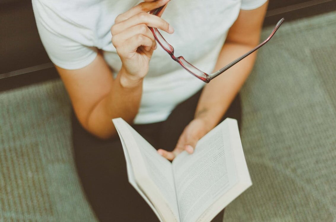 A woman in glasses reads a book intently.