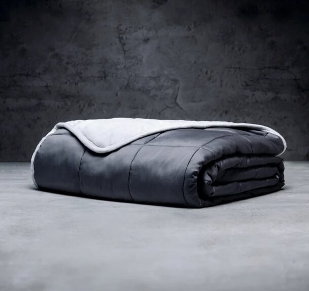 A gray blanket spread out on a concrete floor, showcasing its texture against the hard surface.