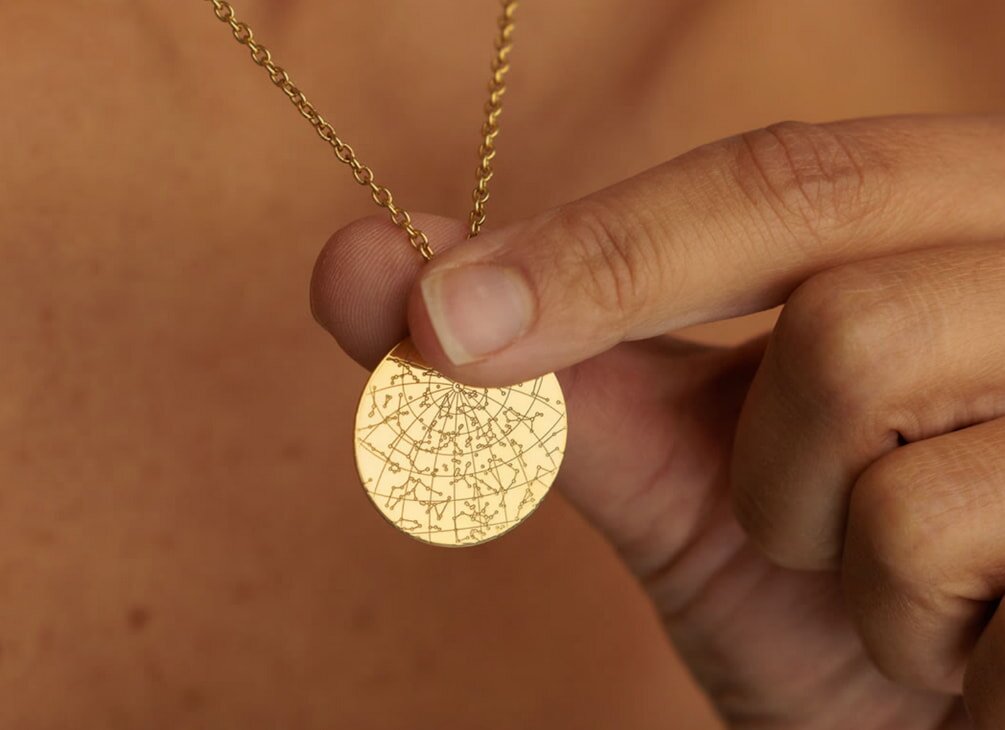 A woman elegantly displays a gold disc necklace, showcasing its shine and design against a neutral background.