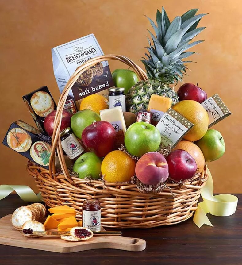 A wicker gift basket brimming with fresh fruits like apples, oranges, a pineapple, and a peach, alongside cookies, cheese, jam, and tea. A warm, inviting presentation.