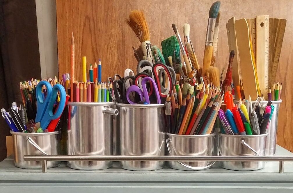 A metal container filled with assorted art supplies, including brushes, paints, and markers, arranged neatly inside.