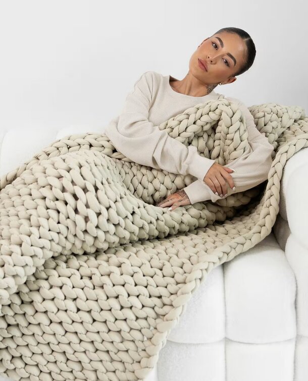 Chunky beige knit blanket draped elegantly, showcasing its soft texture and cozy appearance.