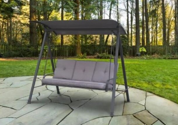 A swing bench in a backyard surrounded by lush green trees in the background, creating a serene outdoor setting.