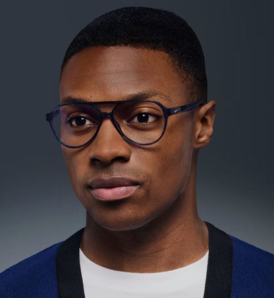 A man with glasses wearing a blue sweater, looking directly at the camera with a neutral expression.