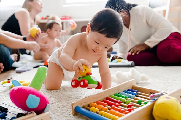 A baby sits on the floor, happily playing with colorful toys scattered around them.