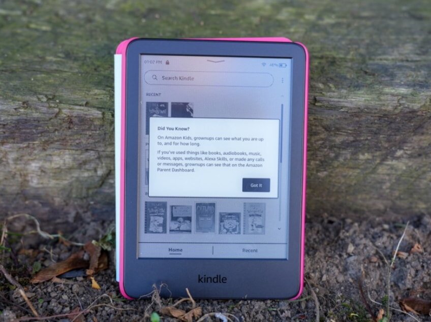 Pink Amazon Kindle e-reader on ground with tree trunk