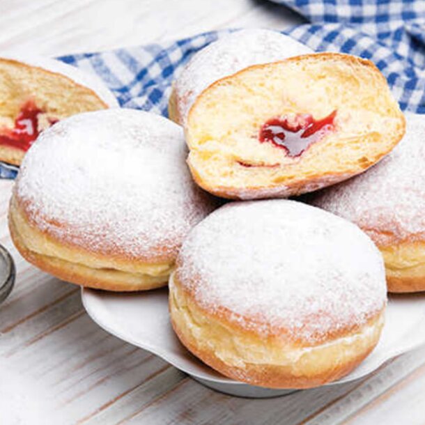 A plate holds several powdered donuts alongside a small dish of jam for dipping.
