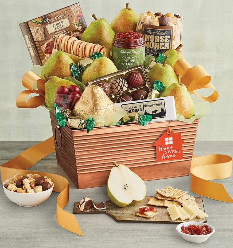 Gift basket with pears, crackers, chocolates, cheese, and jams, adorned with gold ribbons. A red "Home Sweet Home" tag adds a welcoming touch.