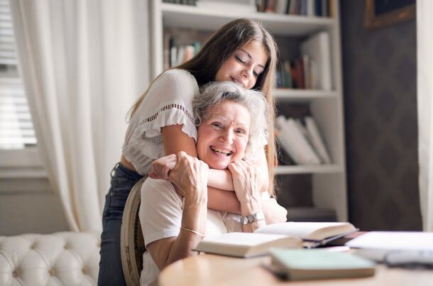 A woman embraces an older woman while seated at a desk, conveying warmth and affection in a shared moment.