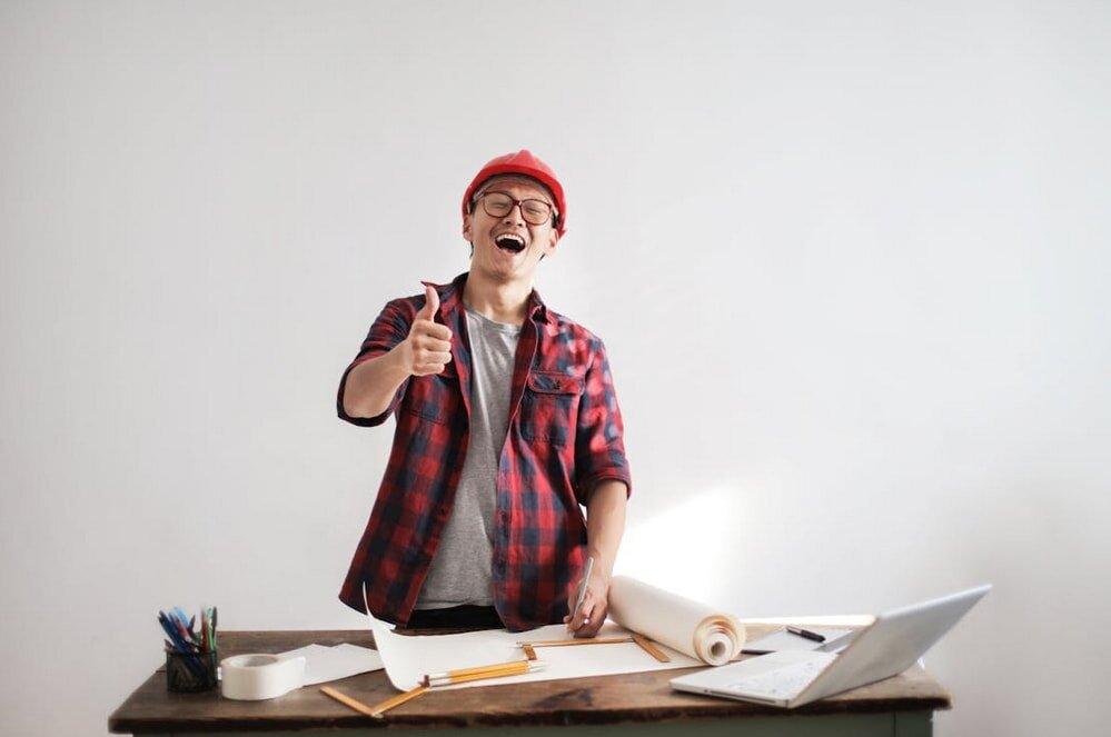 A man wearing a red hat gives a thumbs up, smiling confidently at the camera.