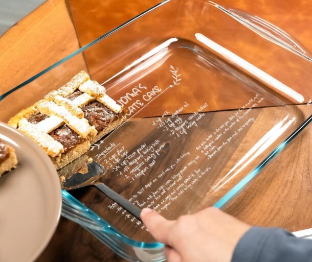 A person slices a cake with a knife, placing the pieces into a glass baking dish.