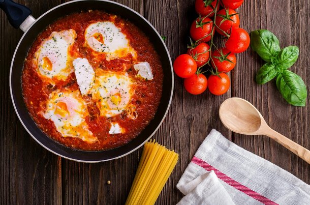 A rustic wooden table displays a vibrant Italian dish featuring eggs and tomatoes.