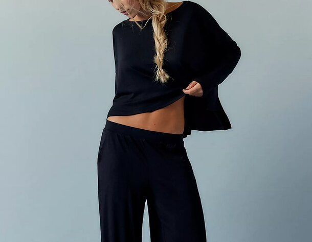 A model showcases a stylish black top paired with wide-legged pants, highlighting a modern fashion look.