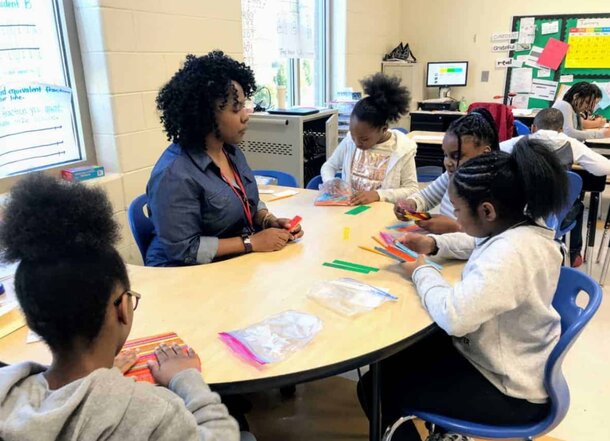 A teacher instructs children at a table in a bright classroom filled with educational materials.