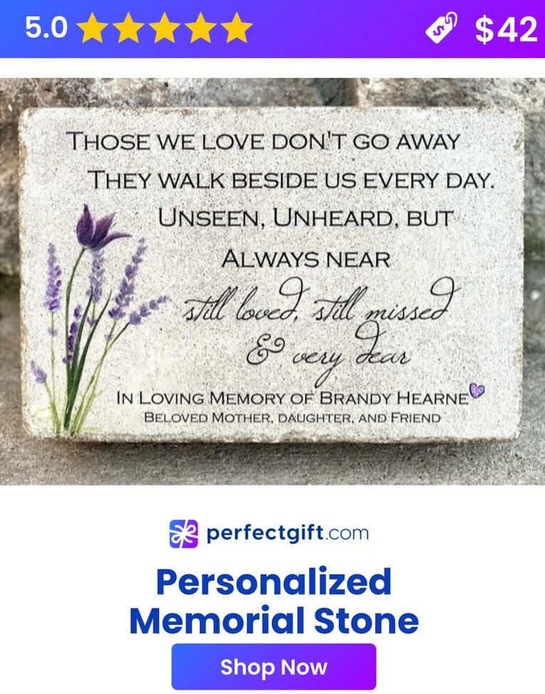 A personalized memorial stone engraved with a name and dates, surrounded by flowers in a serene outdoor setting.  