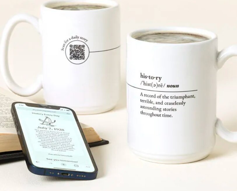 A coffee mug is placed next to a book and an iPhone, indicating a moment of leisure and enjoyment.