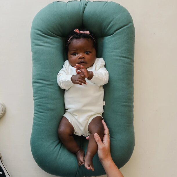 A baby peacefully lying in a green baby bed, surrounded by soft bedding and a cozy atmosphere.