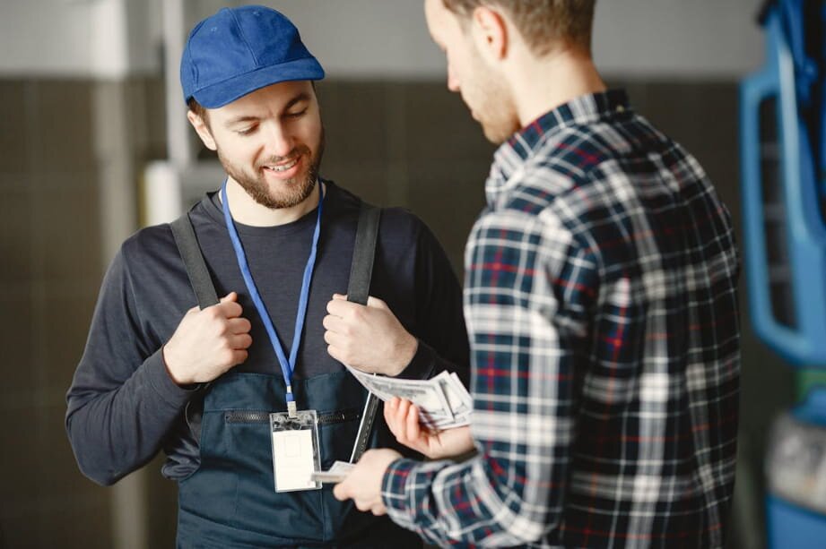 Two men in overalls stand beside a blue car, smiling and engaged in conversation.