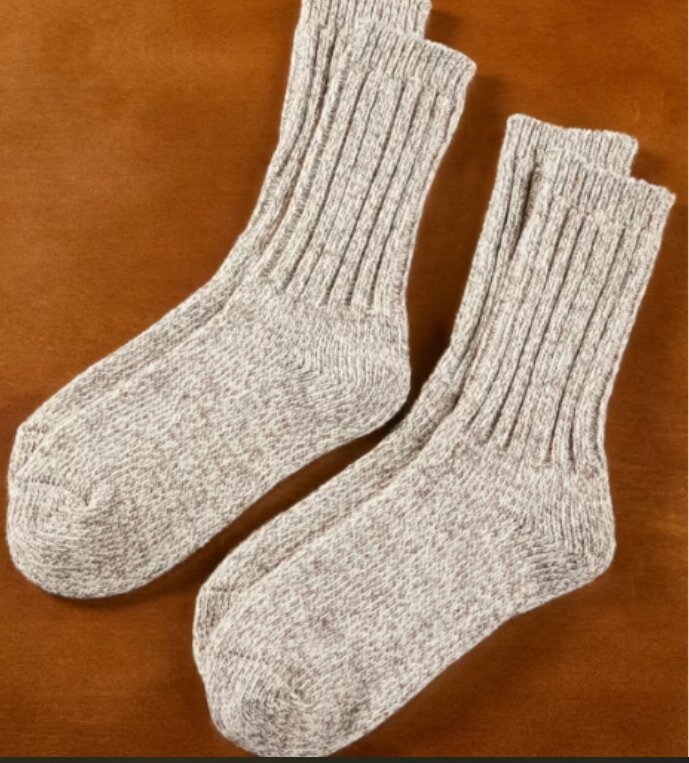 A pair of thick, gray wool socks with ribbed cuffs, lying flat on a warm brown surface. They convey a cozy and comfortable feeling.