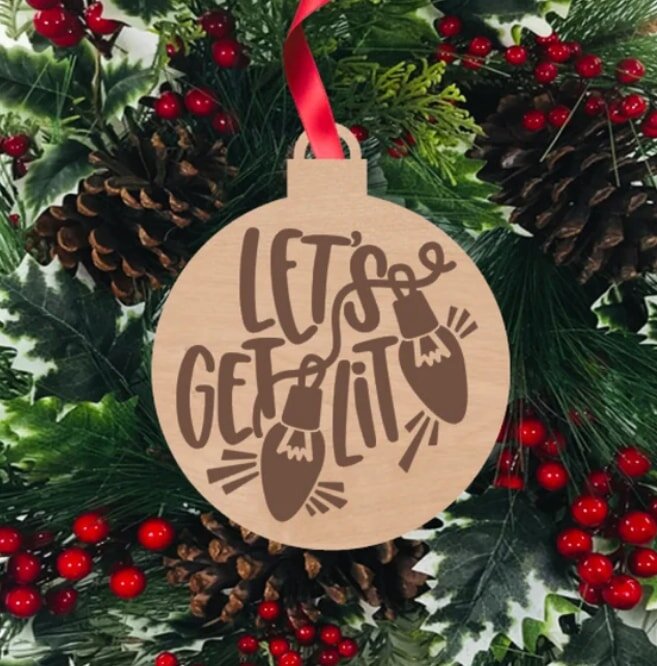 Wooden ornament with "Let's Get Lit" text hangs on a red ribbon, surrounded by pinecones and holly with red berries.
