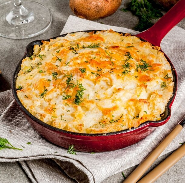 A skillet containing cooked potatoes topped with gooey cheese rests on a rustic table.