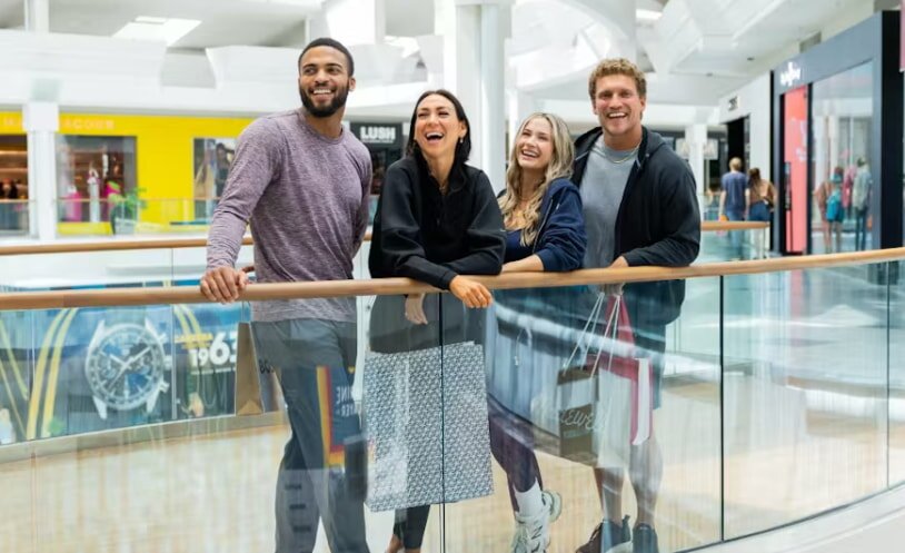 Four people stand in a mall, smiling and looking directly at the camera.