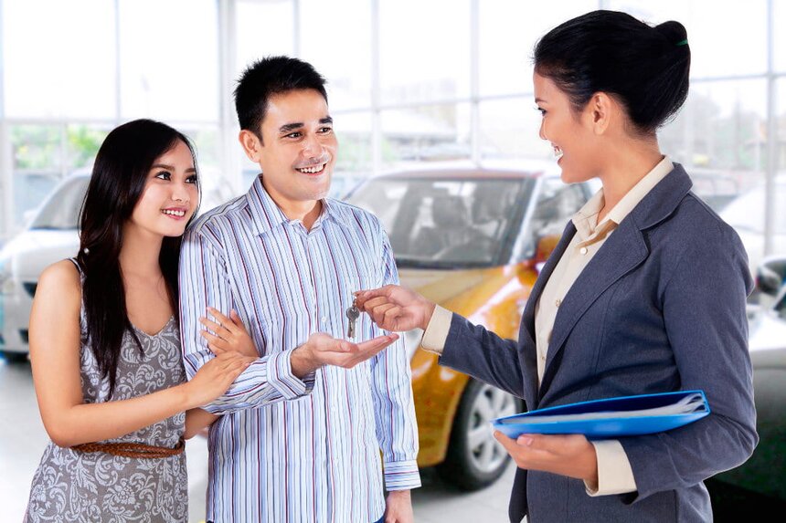 A man and woman stand together in front of a parked car, smiling and engaged in conversation.