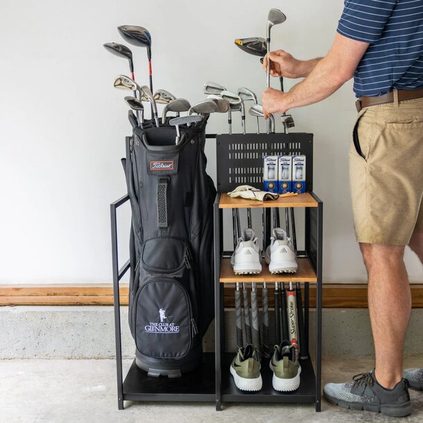 A man stands holding a rack filled with various golf clubs, showcasing his interest in the sport.