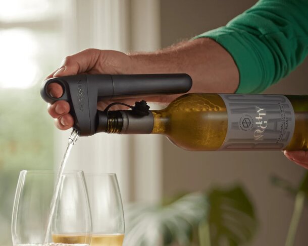 A person pours red wine into a glass while holding a bottle opener in the other hand.