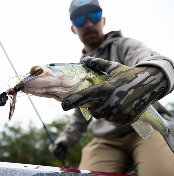 A man wearing a hat and gloves holds a freshly caught fish, smiling proudly at his catch.