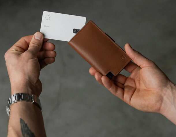 A close-up of two hands gripping a credit card and an open wallet, indicating a financial exchange.