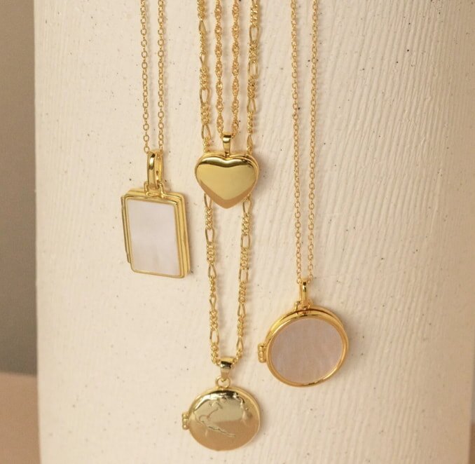 Silver wind chimes with a wooden clapper and engraved tag hang against a blurred, sunlit green garden, evoking a peaceful, serene atmosphere.