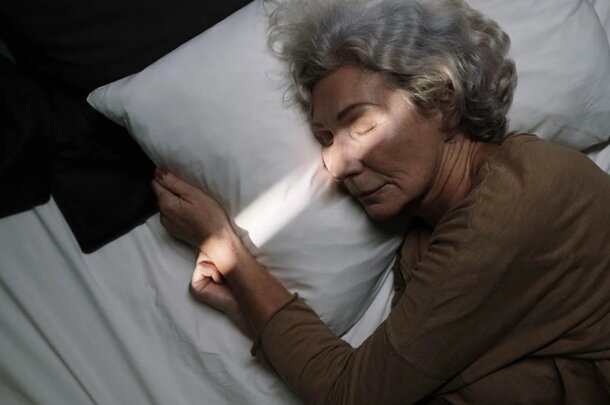 An older woman peacefully sleeping in bed, resting her head on a soft pillow. 