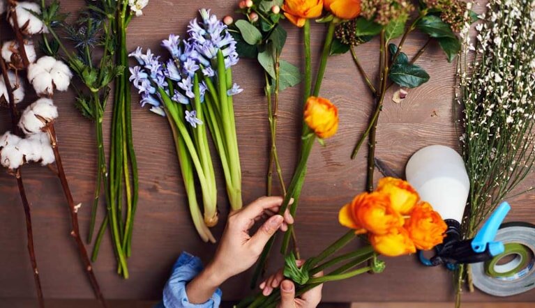 A person carefully arranges colorful flowers on a wooden table, creating an aesthetically pleasing floral display.