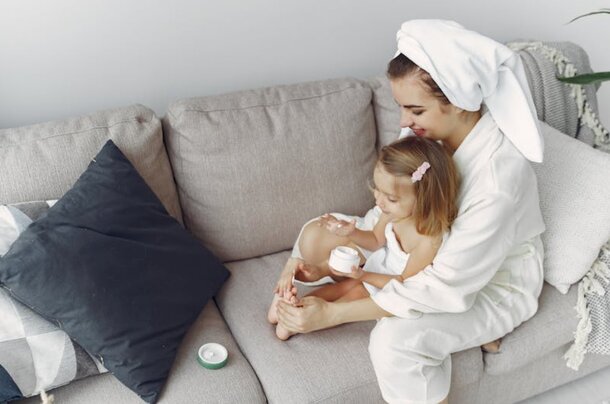 A woman and child relax on a couch, both covered with a towel, enjoying a cozy moment together.