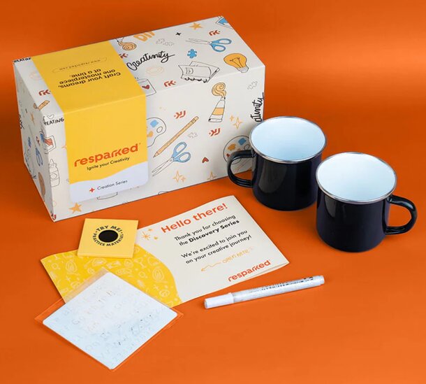Colorful gift box labeled "resparked" with doodles, two black mugs, a note, and a pen on an orange background. Creative and welcoming vibe.