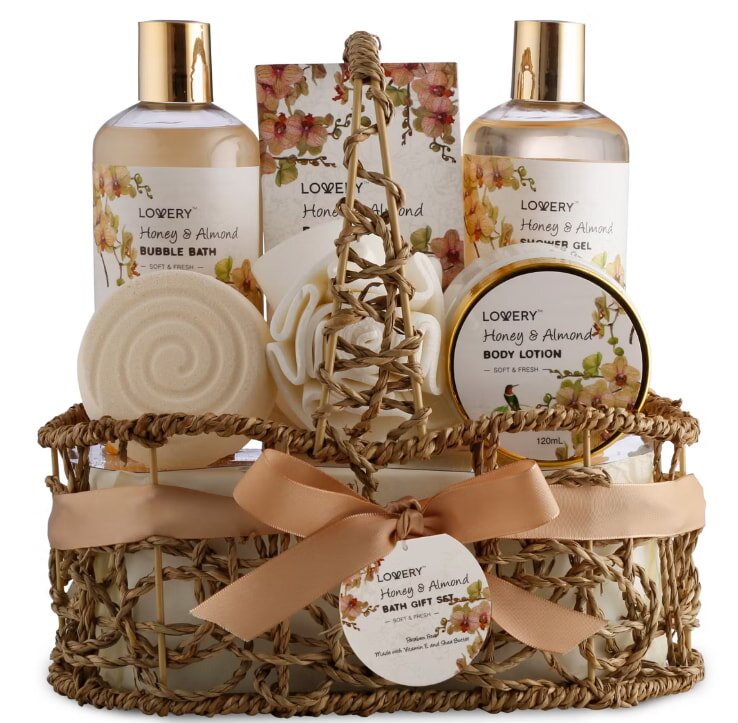 A wicker basket gift set with honey and almond scented bath products, including bubble bath, shower gel, body lotion, and soap, adorned with a peach ribbon.